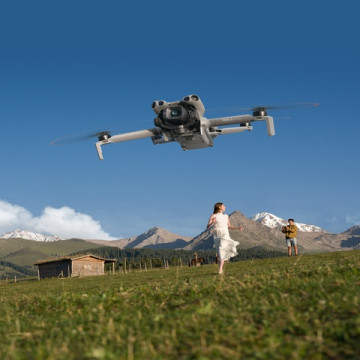 the_dji_mini_5-pro_hovers_in_a_blue_sky_over_a_green_field_in_mounains_a_woman_in_a_white_dress_runs_toward_it DJI.
