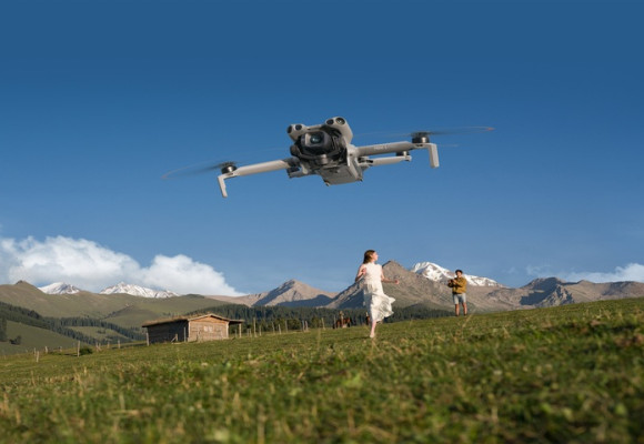 the_dji_mini_5-pro_hovers_in_a_blue_sky_over_a_green_field_in_mounains_a_woman_in_a_white_dress_runs_toward_it DJI.